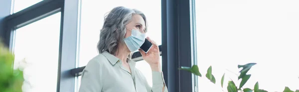 Grey Haired Businesswoman Medical Mask Talking Smartphone Window Office Banner — Stock Photo, Image