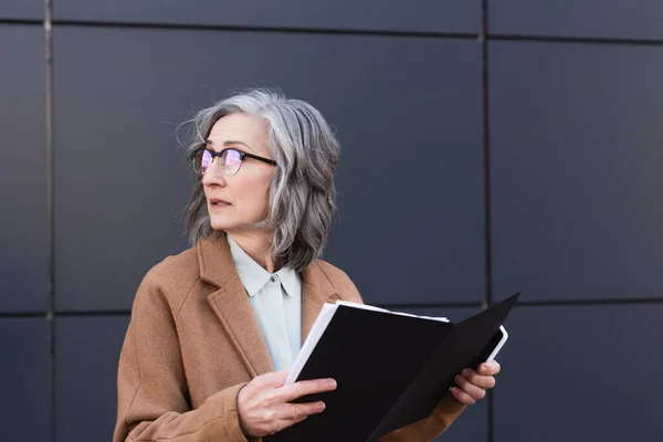 Mature Businesswoman Coat Holding Paper Folder Smartphone While Looking Away — Stock Photo, Image