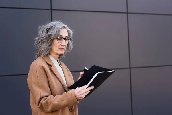 Mature Businesswoman Eyeglasses Coat Holding Paper Folder Cellphone Outdoors — Stock Photo, Image