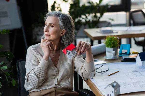 Pensive Businesswoman Trzyma Model Domu Pobliżu Planu Biurze — Zdjęcie stockowe