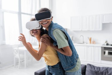 VR kulaklıklı gülümseyen Afro-Amerikan adam evde kız arkadaşına sarılıyor. 