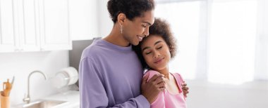 Genç Afro-Amerikalı, gözleri kapalı. Mutfakta kız arkadaşına sarılıyor. 