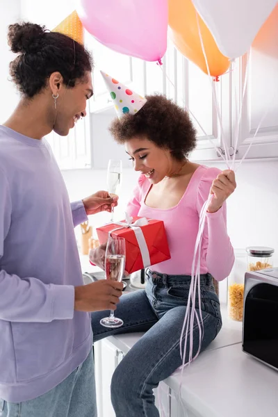 Lächelnde Afroamerikanerin Mit Geschenk Und Luftballons Neben Freund Partymütze Mit — Stockfoto