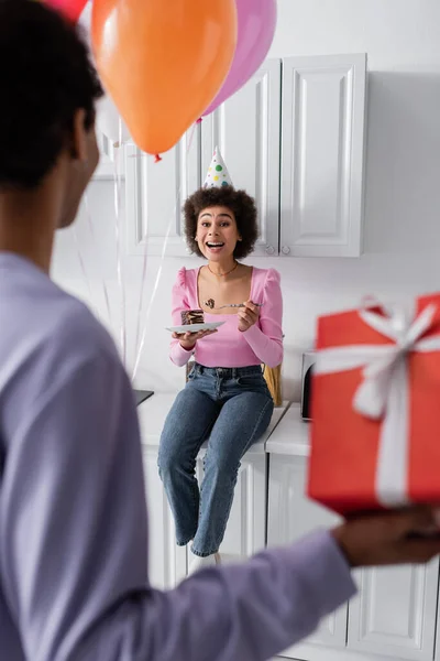 Excited African American Woman Party Cap Holding Cake Blurred Boyfriend — Stockfoto
