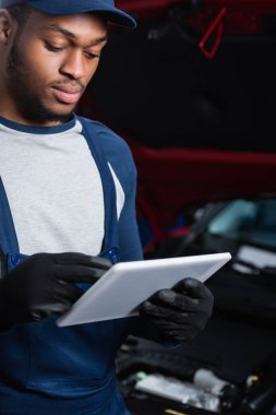 Afrika kökenli iş eldivenli Amerikalı teknisyen araba servisi istasyonunda çalışırken dijital tablet kullanıyor.