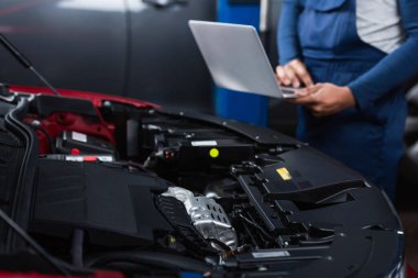 Araba motoru kompartımanının yanında dizüstü bilgisayarı olan bulanık Afrikalı Amerikalı tamircinin kısmi görüntüsü 