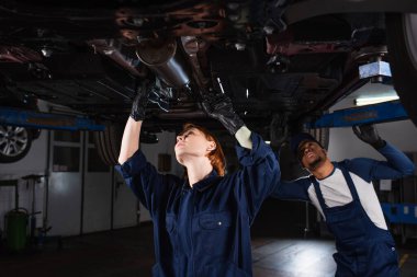 Araç servisindeki kaldırılmış otomobili inceleyen ırklar arası teknisyenler