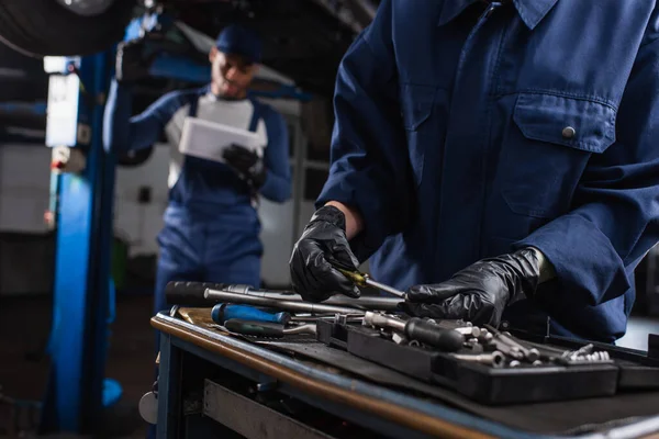 Mekaniker Handskar Tar Verktyg Nära Suddig Afrikansk Amerikansk Kollega Garage — Stockfoto