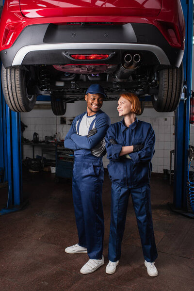 Multiethnic mechanics looking at each other under car in service 