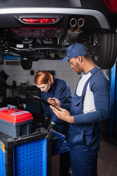 African American Workman Holding Clipboard While Colleague Working Toolbox Car — Stock Photo, Image