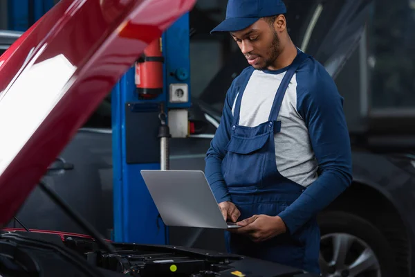 Joven Afroamericano Técnico Utilizando Portátil Cerca Coche Con Capucha Abierta —  Fotos de Stock