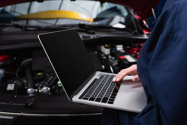 partial view of forewoman with laptop making diagnostics of blurred car in service