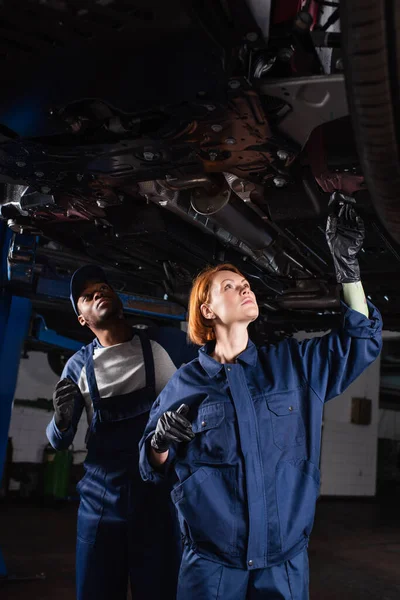 Interracial Workers Car Service Inspecting Bottom Lifted Auto Workshop — Stock Photo, Image