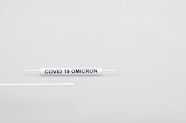 swab test near blurred covid-19 omicron test tube on grey background