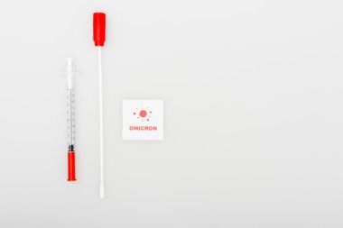 top view of card with omicron lettering and bacteria icon near swab test and syringe on grey background