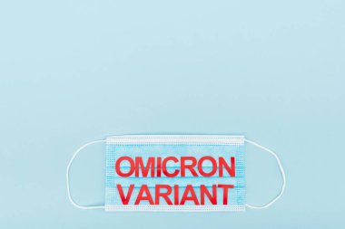top view of medical mask with red omicron variant lettering on blue background with copy space