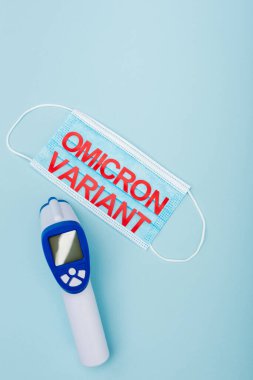 top view of medical mask with omicron lettering near pyrometer on blue