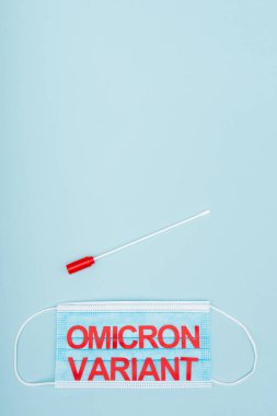 top view of swab test near medical mask with red omicron variant lettering on blue