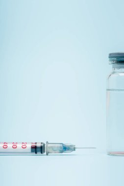 close up view of vaccine bottle near syringe on blue background, omicron variant concept