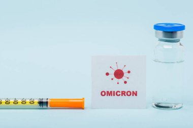 card with omicron lettering near syringe and vaccine vial on blue background