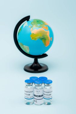 covid-19 omicron variant vaccine bottles near blurred globe on blue background clipart