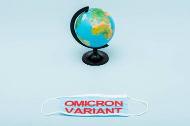medical mask with red omicron variant lettering near globe on blue background