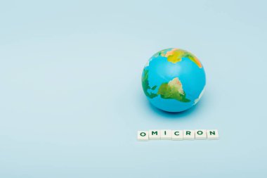 white cubes with omicron lettering near globe on blue background with copy space