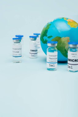 covid-19 and omicron strain vaccine jars near globe on blue