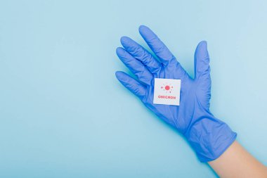 cropped view of doctor in latex glove holding white card with red omicron lettering and bacteria on blue