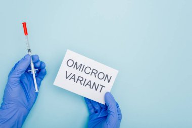 cropped view of doctor holding syringe and card with omicron variant lettering on blue
