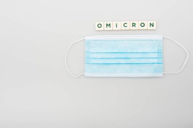 top view of medical mask near white cubes with omicron lettering on grey background