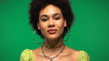 Küpeli kıvırcık Afrikalı Amerikalı kadın yeşil kameraya bakıyor. 