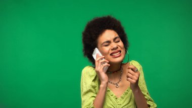 Bluzlu, stresli Afrikalı Amerikalı kadın yeşil odada cep telefonuyla konuşuyor.