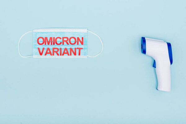 top view of medical mask with red omicron variant lettering near pyrometer on blue