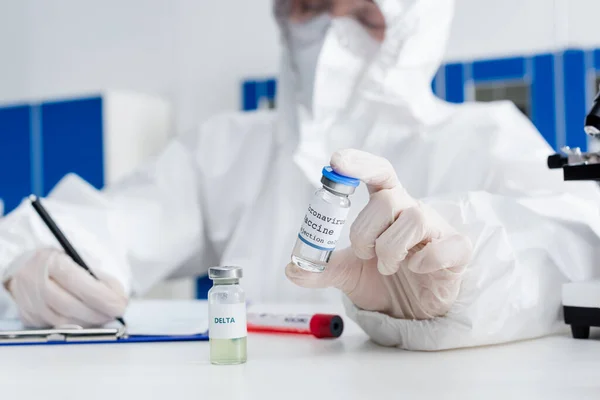 Blurred Doctor Hazmat Suit Holding Coronavirus Vaccine While Writing Clipboard — Stok Foto