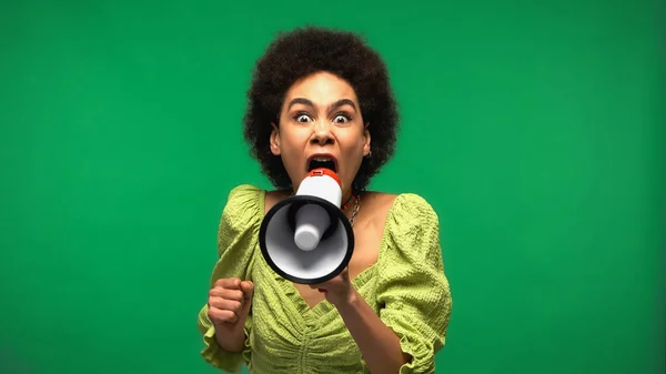 angry african american woman screaming in loudspeaker and looking at camera isolated on green