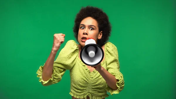 angry african american woman protesting while holding loudspeaker and looking at camera isolated on green