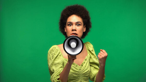 irritated african american woman protesting while holding loudspeaker and looking at camera isolated on green 