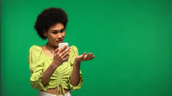 Mulher Afro Americana Insatisfeita Olhando Para Smartphone Isolado Verde — Fotografia de Stock