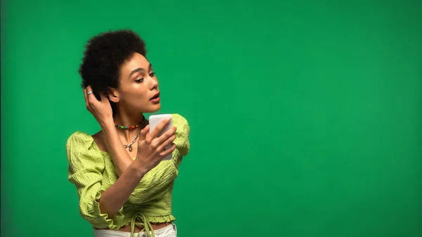 身穿女衫的非洲裔美国女人 看着智能手机 调整被绿色隔离的头发 — 图库照片