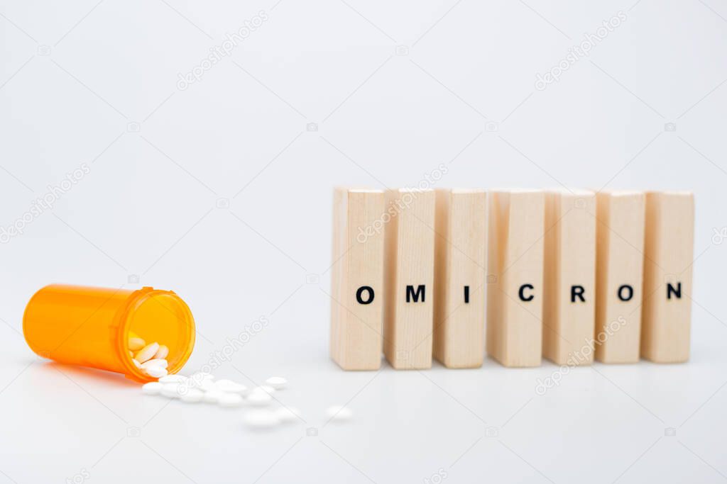 wooden bricks with omicron lettering near pills on grey background