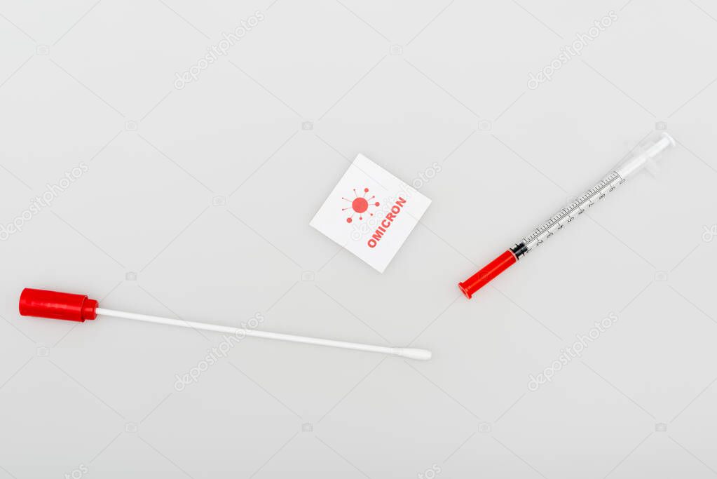 top view of card with omicron lettering and bacteria near swab test and syringe on grey 