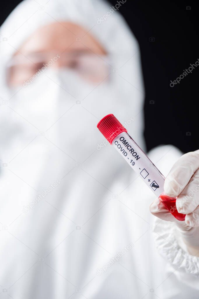 close up view of positive covid-19 omicron variant test in hand of blurred doctor in hazmat suit isolated on black