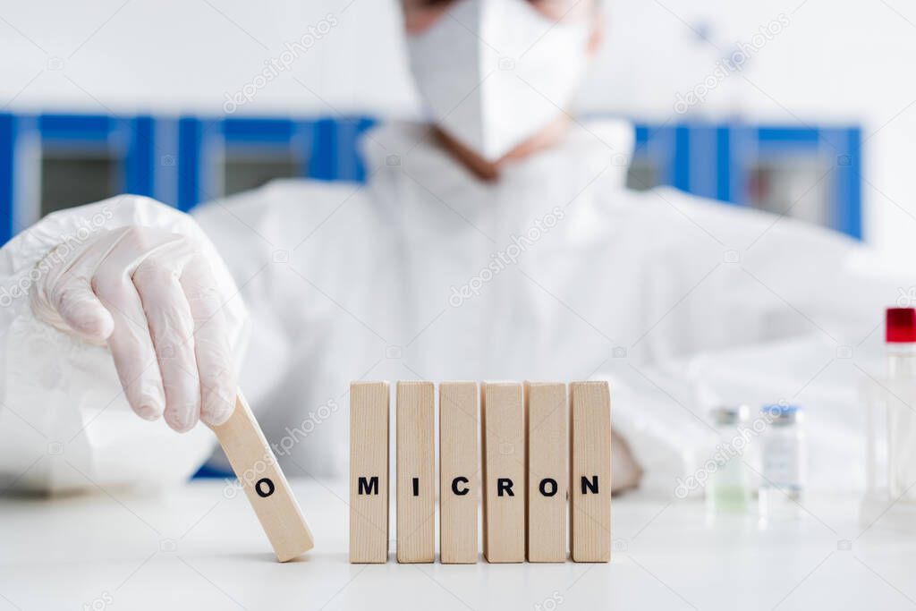 cropped view of wooden bricks in hazmat suit near blocks with omicron lettering in lab