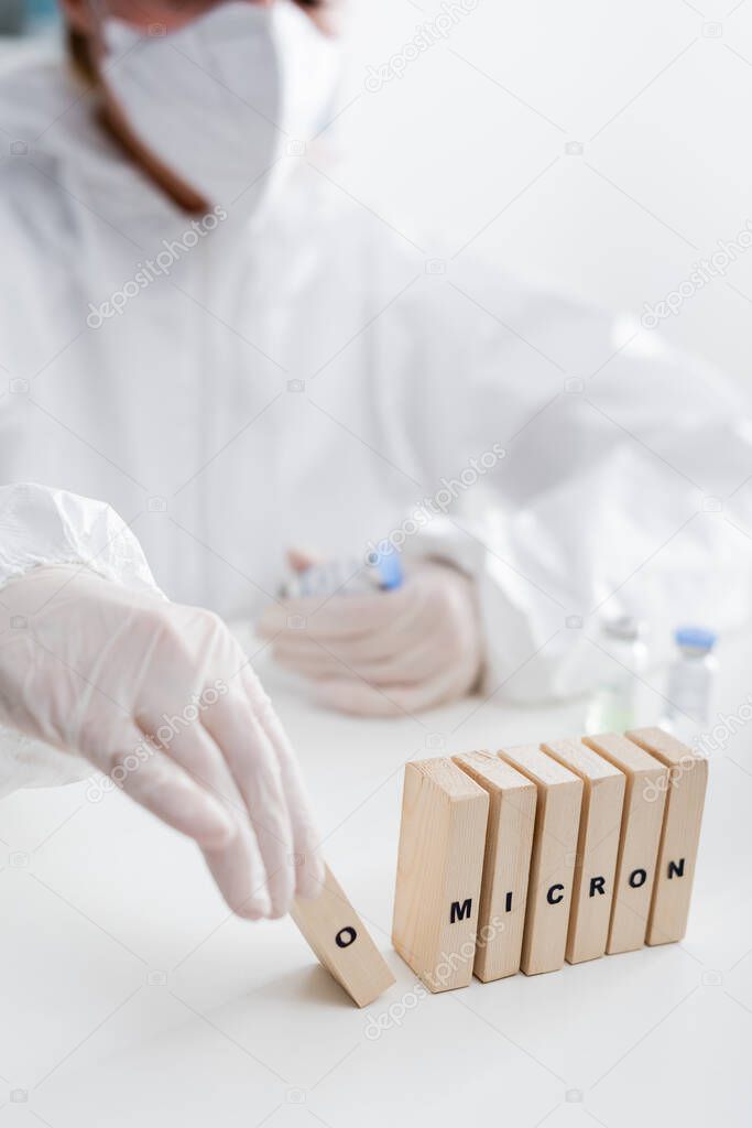 partial view of blurred immunologist near vaccine vials and wooden bricks with omicron lettering