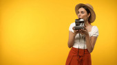 Excited tourist in straw hat holding vintage camera isolated on yellow