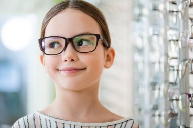 girl in eyeglasses smiling in optics store on blurred background
