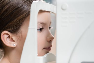 girl measuring eyesight on blurred ophthalmoscope  clipart