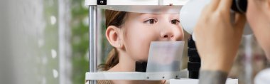 blurred oculist checking eyesight of girl on vision screener in optics shop, banner clipart