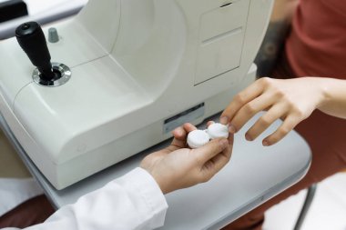 partial view of optometrist giving lens case to patient near autorefractor